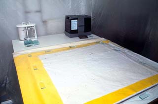 Abb. 1: Abdeckung eines textilen Objekts mit Laminat (hier gelb), feuchtem Gewebe (hier weiß) und Polyethylenfolie im Arbeitszelt mit Luftbefeuchter und Thermohygrograph